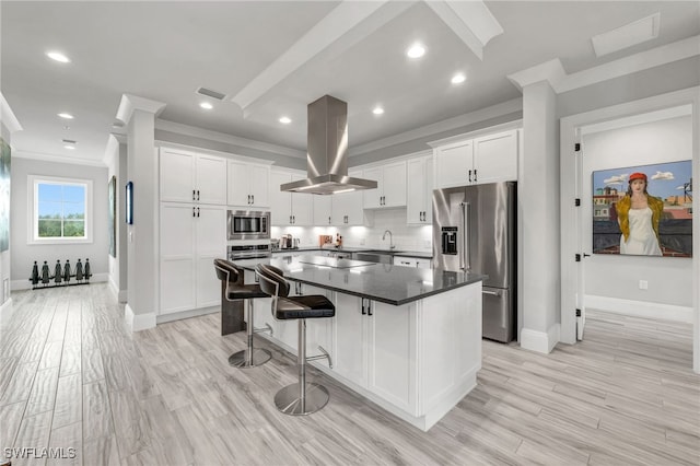 kitchen featuring a center island, white cabinets, island range hood, appliances with stainless steel finishes, and ornamental molding