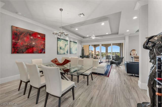 dining space featuring light wood-type flooring, ornamental molding, a tray ceiling, and a chandelier