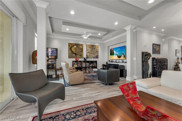 living room with a tray ceiling, decorative columns, light hardwood / wood-style flooring, ornamental molding, and ceiling fan