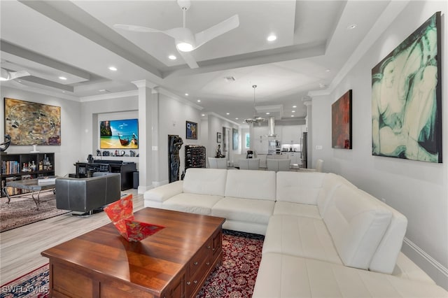 living room featuring ceiling fan with notable chandelier, decorative columns, crown molding, and a tray ceiling