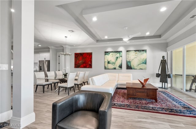 living room featuring light wood-type flooring, ceiling fan with notable chandelier, and a raised ceiling