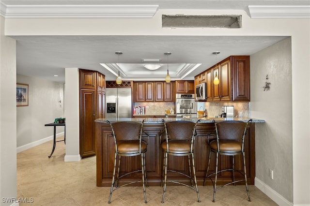 kitchen featuring kitchen peninsula, hanging light fixtures, stainless steel appliances, a raised ceiling, and dark stone countertops