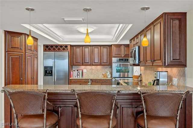 kitchen featuring stainless steel appliances, light stone counters, a raised ceiling, and hanging light fixtures