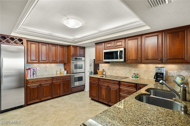 kitchen featuring decorative backsplash, light stone counters, a raised ceiling, stainless steel appliances, and sink