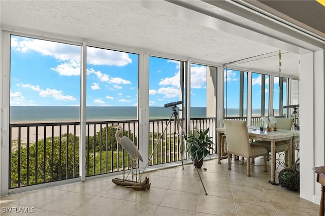 unfurnished sunroom featuring a healthy amount of sunlight, a water view, and a beach view