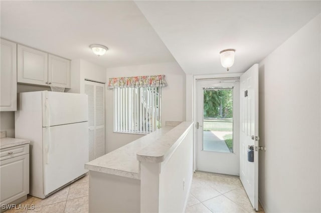 kitchen with white refrigerator, light tile patterned flooring, and white cabinets