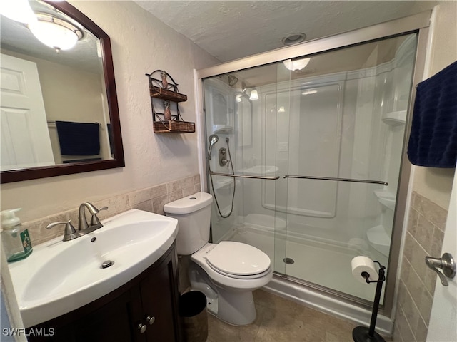 bathroom featuring vanity, an enclosed shower, a textured ceiling, tile walls, and toilet