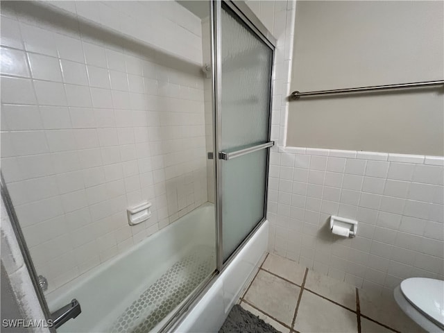 bathroom with tile walls, tile patterned flooring, shower / bath combination with glass door, and toilet