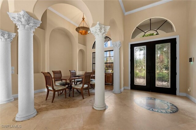 tiled entrance foyer featuring french doors, ornamental molding, ornate columns, and a high ceiling