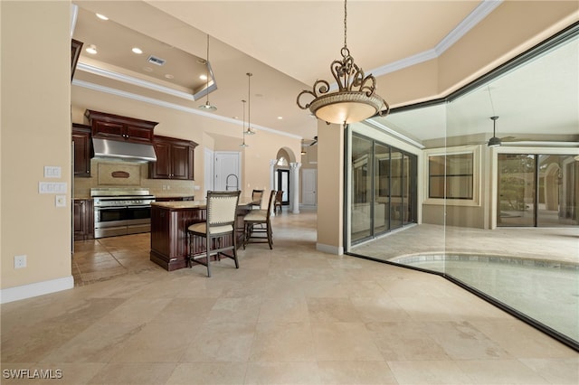 kitchen featuring ceiling fan, hanging light fixtures, a kitchen island with sink, stainless steel range, and a kitchen bar