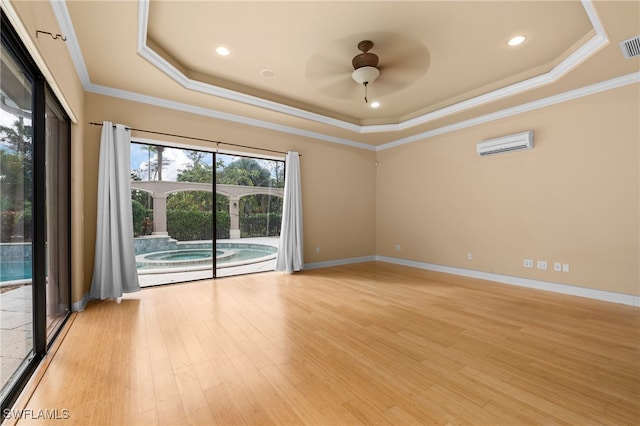 spare room with light wood-type flooring, a tray ceiling, ceiling fan, a wall unit AC, and ornamental molding