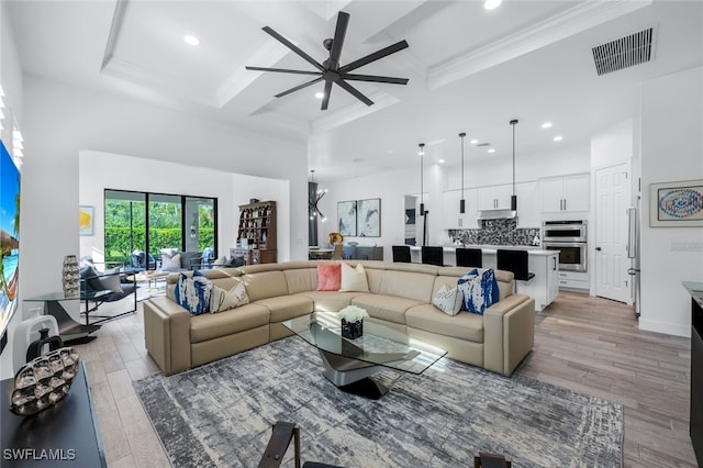 living room with light wood-type flooring, beam ceiling, crown molding, ceiling fan, and coffered ceiling