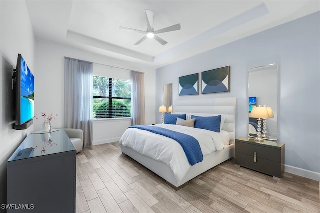 bedroom featuring ceiling fan, a tray ceiling, and light hardwood / wood-style floors