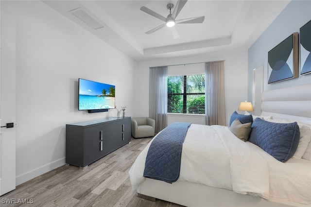 bedroom with light wood-type flooring, ceiling fan, and a tray ceiling