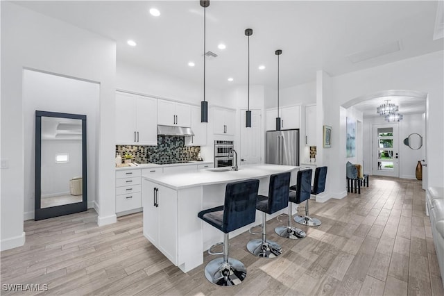 kitchen with sink, decorative light fixtures, white cabinetry, an island with sink, and appliances with stainless steel finishes