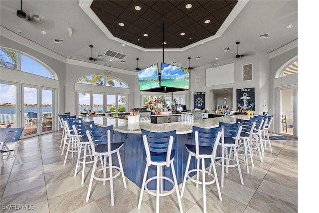 kitchen with ceiling fan, a large island with sink, a high ceiling, a tray ceiling, and crown molding