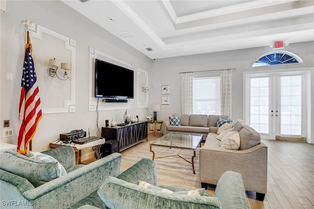 living room with french doors, light wood-type flooring, and a raised ceiling