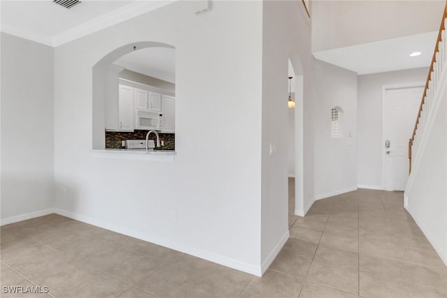 hall with arched walkways, crown molding, stairway, light tile patterned flooring, and baseboards