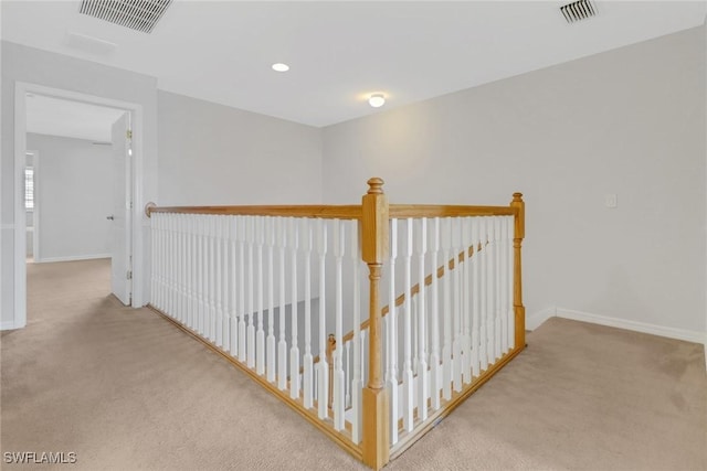 corridor with carpet floors, visible vents, and an upstairs landing