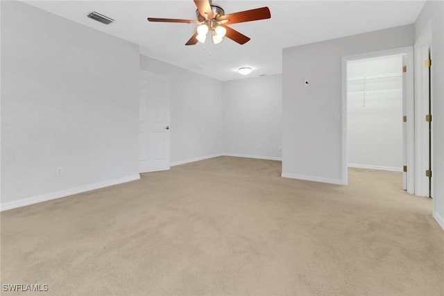 empty room with baseboards, visible vents, ceiling fan, and light colored carpet