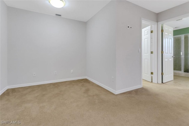 spare room featuring light colored carpet, visible vents, and baseboards