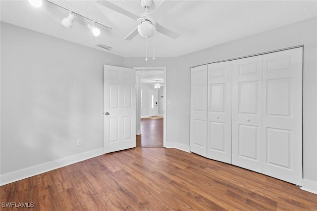 unfurnished bedroom with a textured ceiling, track lighting, a closet, hardwood / wood-style flooring, and ceiling fan