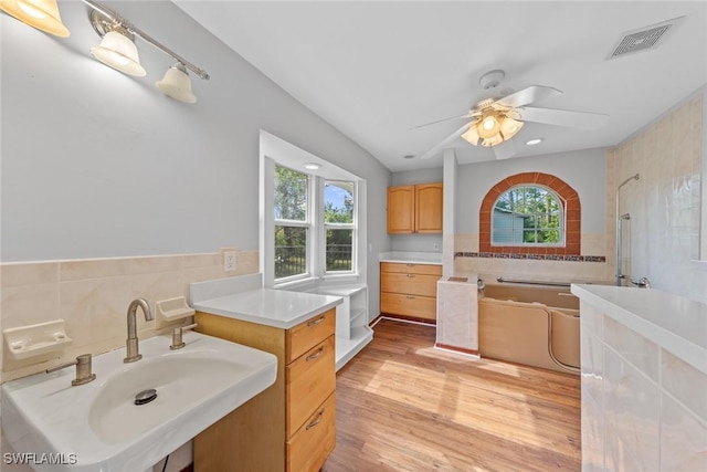 bathroom with sink, hardwood / wood-style flooring, ceiling fan, tile walls, and a bath