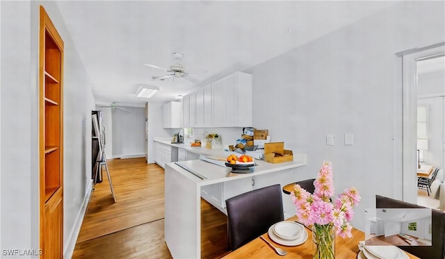 kitchen featuring light hardwood / wood-style flooring, a breakfast bar area, ceiling fan, white cabinetry, and kitchen peninsula