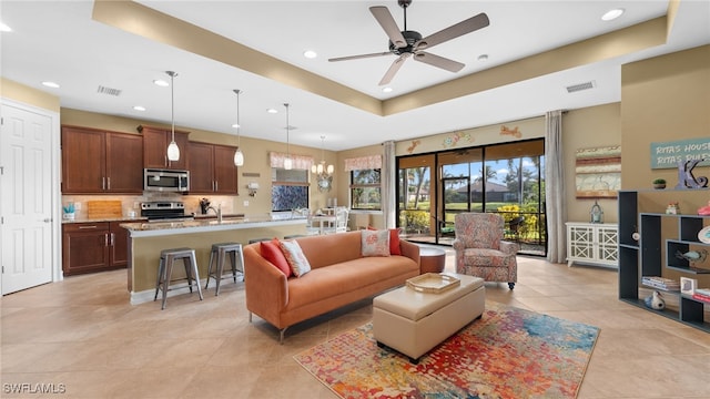 living room with light tile patterned floors, ceiling fan with notable chandelier, and a raised ceiling