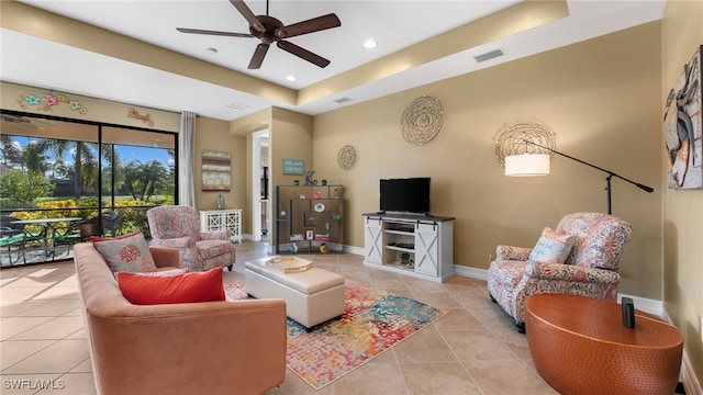 living room with ceiling fan, light tile patterned flooring, and a tray ceiling