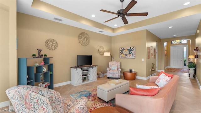 tiled living room with a tray ceiling and ceiling fan