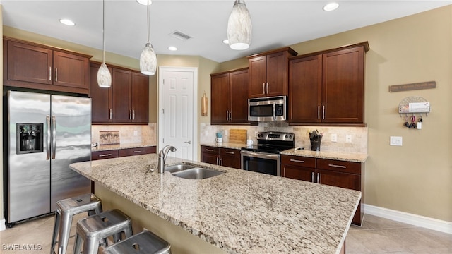 kitchen with sink, an island with sink, pendant lighting, a breakfast bar area, and appliances with stainless steel finishes