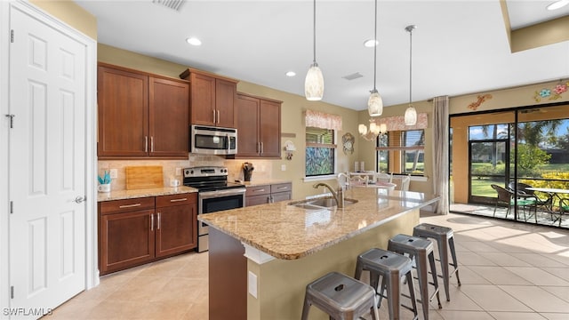 kitchen with a breakfast bar, a center island with sink, hanging light fixtures, sink, and appliances with stainless steel finishes