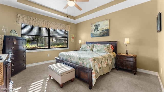 carpeted bedroom with ceiling fan and a raised ceiling