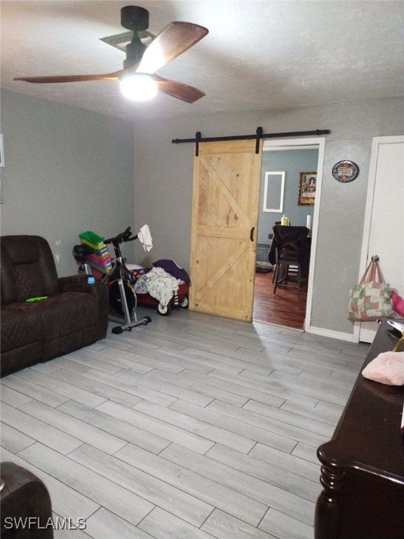 living room featuring a barn door, ceiling fan, and light hardwood / wood-style flooring