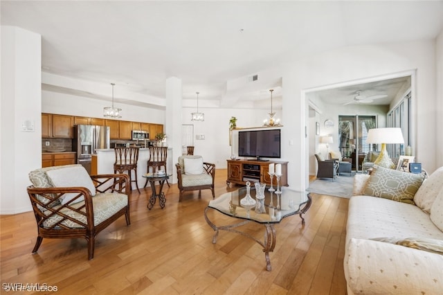 living room featuring lofted ceiling, ceiling fan with notable chandelier, and light hardwood / wood-style flooring