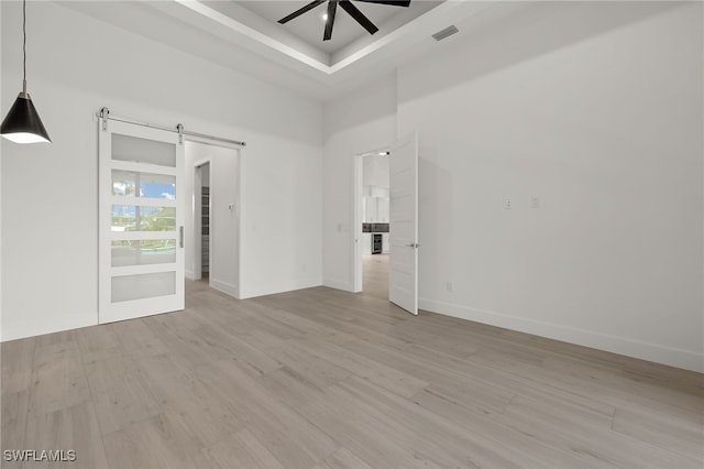 unfurnished room with light hardwood / wood-style flooring, a barn door, and ceiling fan