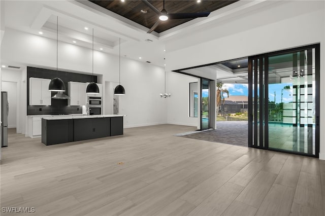 kitchen featuring stainless steel fridge, white cabinetry, a kitchen island with sink, light hardwood / wood-style flooring, and pendant lighting