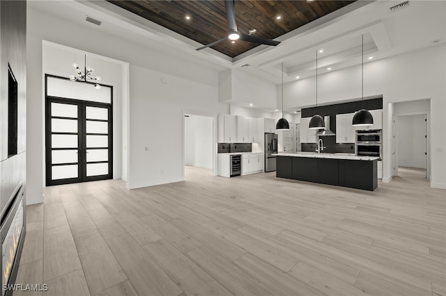 kitchen featuring french doors, a kitchen island with sink, pendant lighting, light wood-type flooring, and a towering ceiling