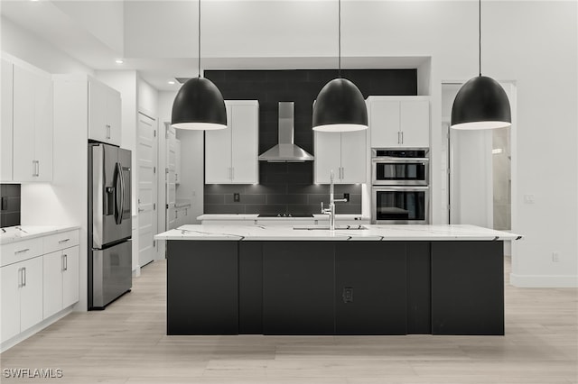 kitchen featuring stainless steel appliances, wall chimney range hood, pendant lighting, and an island with sink