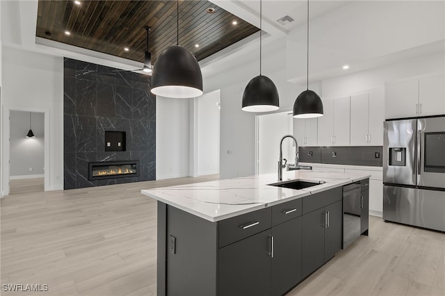 kitchen with white cabinets, hanging light fixtures, a kitchen island with sink, stainless steel refrigerator with ice dispenser, and sink