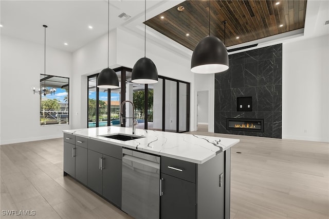 kitchen featuring an island with sink, a tray ceiling, sink, decorative light fixtures, and stainless steel dishwasher