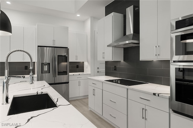 kitchen with light stone countertops, white cabinets, wall chimney range hood, and stainless steel appliances