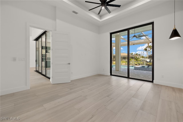 unfurnished room with a tray ceiling, light wood-type flooring, and ceiling fan