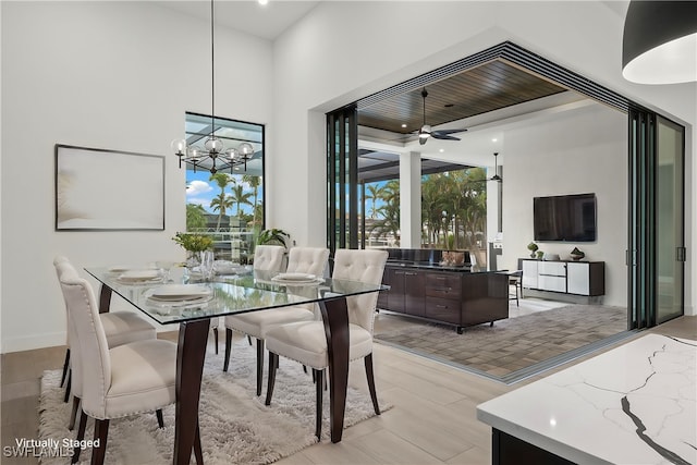 dining area with a high ceiling, light wood-type flooring, and ceiling fan with notable chandelier