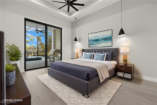 bedroom with a towering ceiling, light hardwood / wood-style flooring, access to exterior, and a tray ceiling