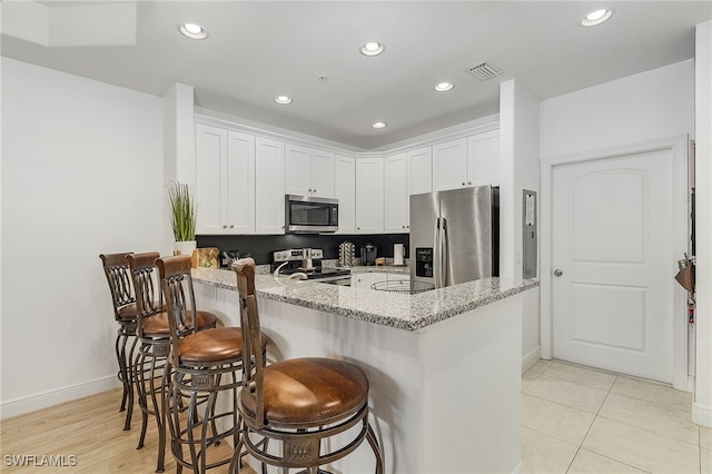 kitchen with a kitchen bar, stainless steel appliances, light stone counters, and white cabinetry