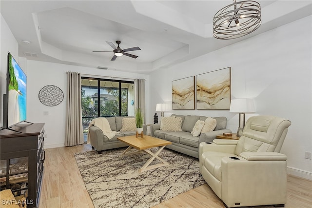 living room with ceiling fan, light hardwood / wood-style floors, and a tray ceiling