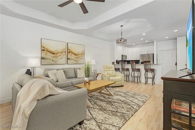 living room featuring ceiling fan, light hardwood / wood-style floors, and a raised ceiling