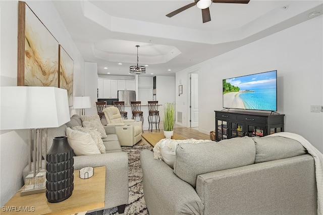 living room featuring a raised ceiling, ceiling fan, and light wood-type flooring